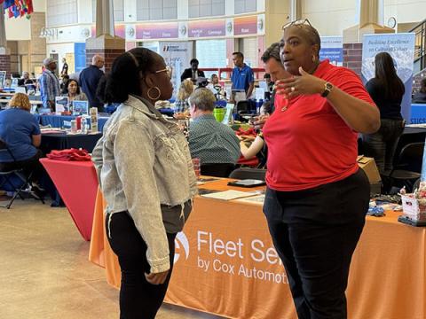 Two women talk in front of the Cox Automotive booth at a hiring fair in Tacoma.