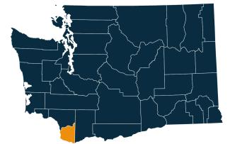 A dark blue map of Washington state with Clark County highlighted in orange