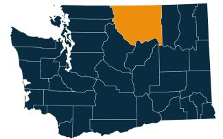 A dark blue map of Washington state with Okanogan County highlighted in orange.