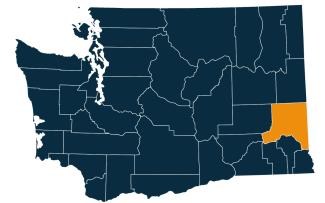 A dark blue map of Washington state with Whitman County highlighted in orange.