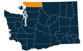 A dark blue map of Washington state with Whatcom County highlighted in orange.