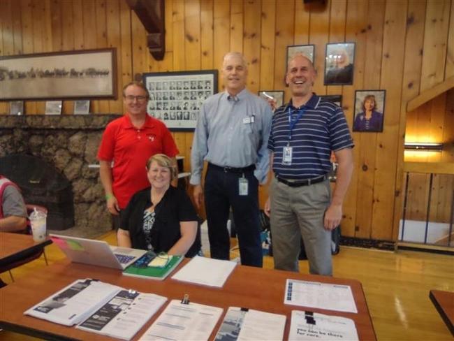 Four Disaster Assistance Center staff members, three standing and one sitting, appear behind a table