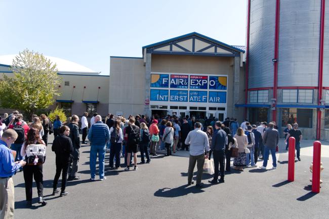 Job seekers line up outside the location of the Spokane Career Fair & Expo on a sunny day.