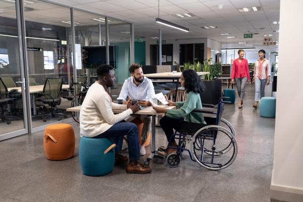 Office environment featuring three people sitting together, one is a wheelchair user